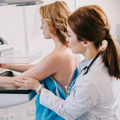 Médica ajudando a paciente a realizar o exame de mamografia na Global exames